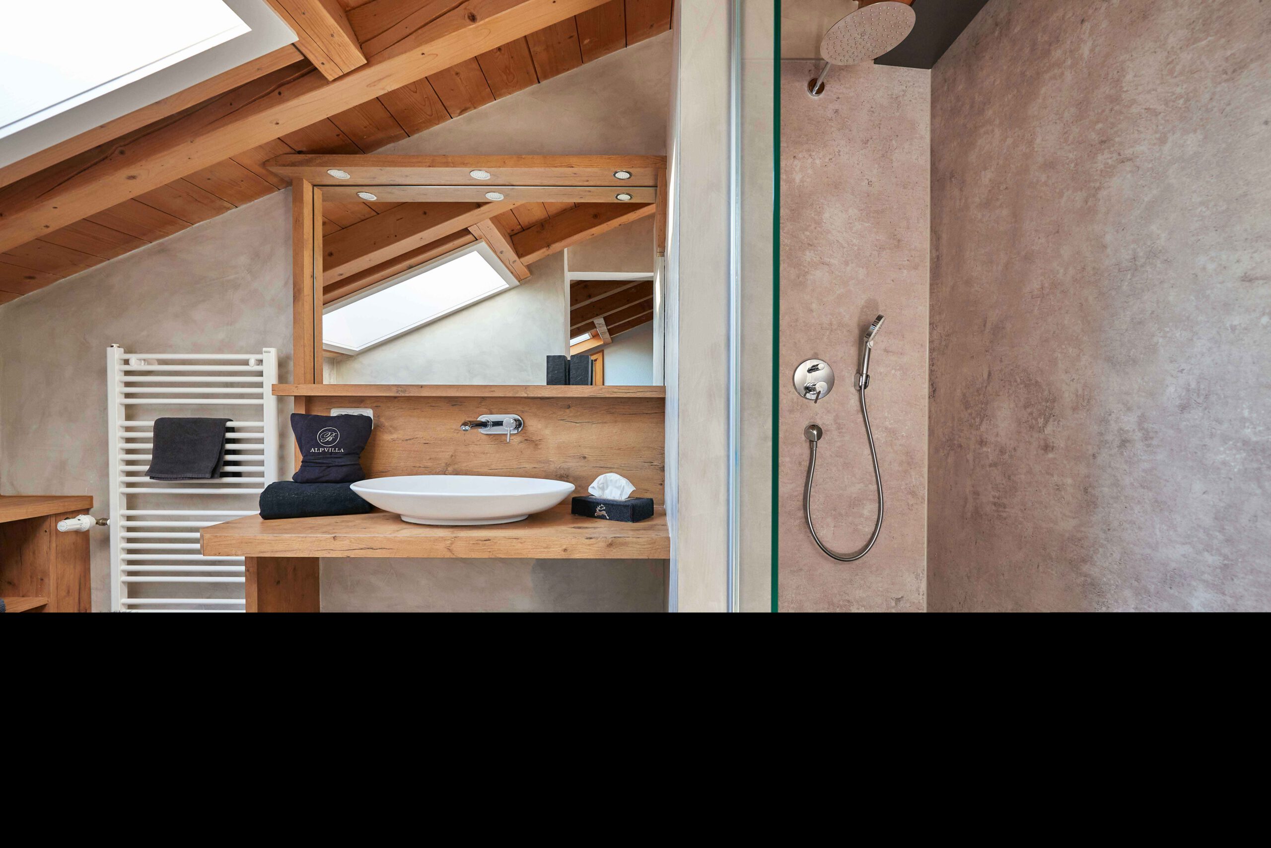 Badezimmer „Almrausch“ mit Waschbecken und großem Spiegel auf der linken Seite und Dusche auf der rechten Seite getrennt durch eine Glaswand.